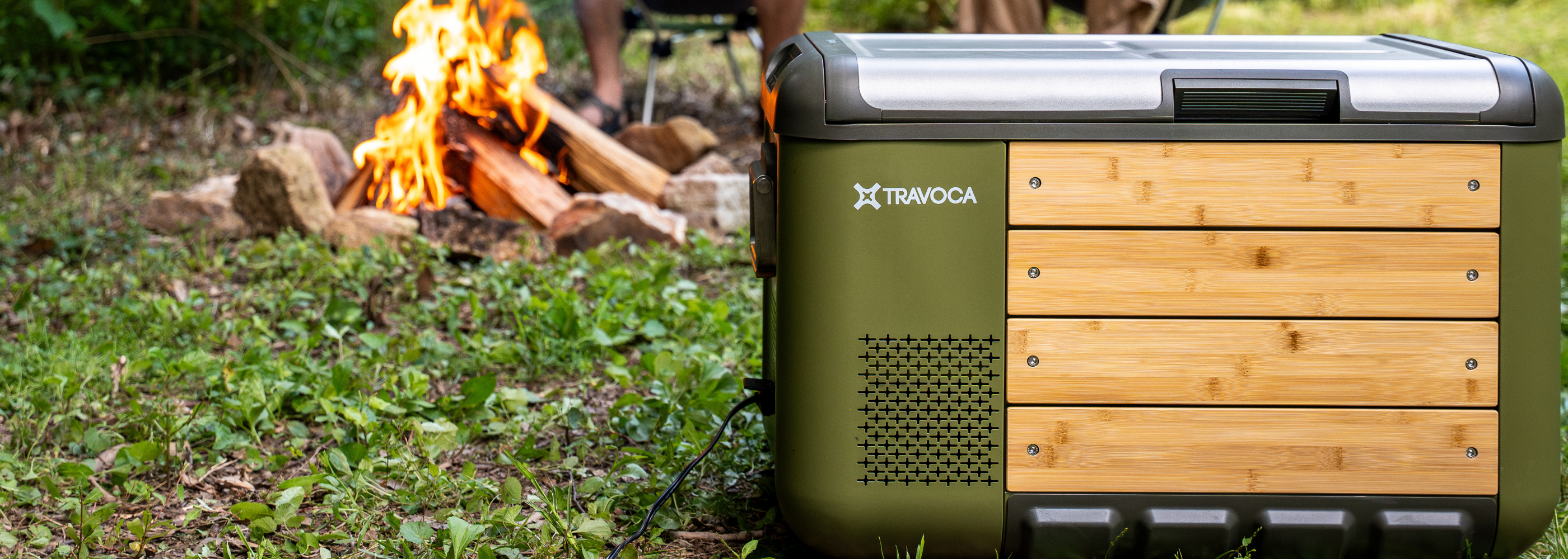TRAVOCA Rigle 35 Dual zone portable eCooler for camping, eco-friendly outdoor refrigerator beside campfire in forest.